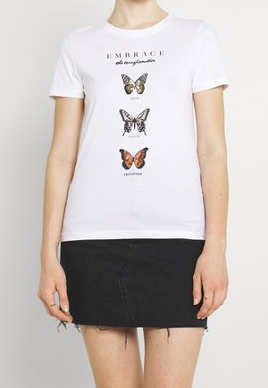 T-shirt bianca a maniche corte con tre farfalle e le parole "embrace the transformation," "grow," "evolve," e "transform", indossata con una gonna di jeans nera.