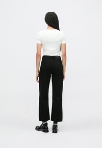 Czarne spodnie o szerokich nogawkach z tylnymi kieszeniami, połączone z dopasowanym białym topem z krótkim rękawem. Modelka nosi czarne buty z połyskującym wykończeniem.