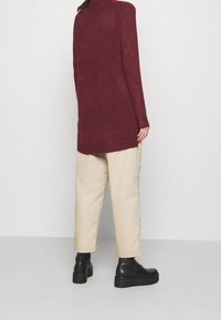 Burgundy long-sleeve sweater in a soft knit, paired with cream tapered pants and black chunky-heeled boots. Simple, relaxed silhouette.