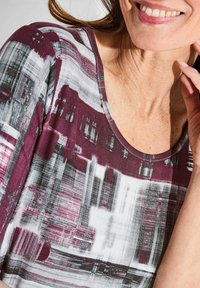 Haut à manches courtes avec un motif abstrait maroon, gris et blanc. L'encolure est en forme de scoop, avec un tissu doux et texturé.