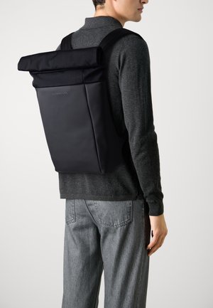 Zaino roll-top nero realizzato in materiale resistente, dotato di spallacci regolabili, design elegante e un discreto dettaglio con logo.
