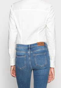 Person wearing a white long-sleeve shirt tucked into high-waisted blue denim jeans with back pockets and a leather brand patch.