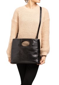 Borsa a tracolla in pelle nera con finitura liscia, forma rettangolare e manico con taglio circolare. La tracolla è regolabile per essere indossata a tracolla.