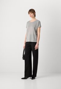 Grijs metallic top met korte mouwen, gecombineerd met zwarte wijde broek en zwarte puntige hakken. Model houdt een kleine zwarte tas vast.