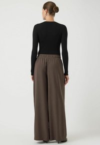 Zwarte ribben top met lange mouwen, gecombineerd met high-waisted, wijde bruine broeken met een elastische tailleband en subtiele textuur.