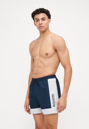 Morske kupaće gaće napravljene od lagane tkanine, s bočnim bijelim panelima i logotipom "CALVIN KLEIN". Elastična pojas s vezicom.