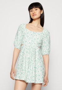 Vestido mini floral em verde claro e branco. Apresenta decote quadrado, mangas bufantes e recortes laterais. Tecido suave e leve.