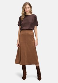 Haut satiné marron à manches courtes associé à une jupe midi en daim marron. Look complété par des bottes à talons hauts en imprimé léopard marron.