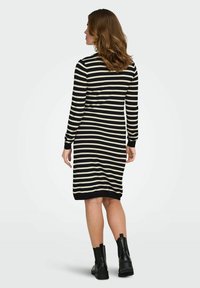 Robe rayée noire et crème à manches longues, col rond et coupe ajustée, portée avec des bottines noires.