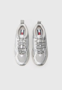 Silver athletic shoes with a mesh upper, metallic accents, elastic laces, and a pull tab on the heel. Interior features contrasting branding.