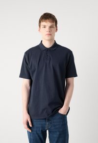 Polo azul marinho com colarinho clássico, três botões e detalhe de logotipo no peito, feita de um tecido de algodão suave.