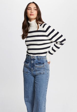 Pull en cachemire à col roulé avec des rayures noir et blanc, associé à un jean bleu taille haute avec des poches plaquées double.