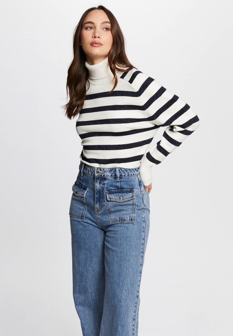 Pull en cachemire à col roulé avec des rayures noir et blanc, associé à un jean bleu taille haute avec des poches plaquées double.