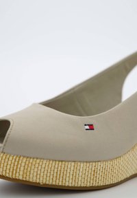 Světle béžová plátěná bota s otevřenou špičkou, tkanou espadrilovou podrážkou a malým vyšitým logem v červené, bílé a modré na boku.