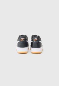 Čierne tenisky Nike Air s bielymi a oranžovými akcentmi, vybavené hladkým koženým vrchom, polstrovanou podrážkou a textúrovanou gumovou podrážkou.