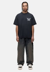 Zwarte katoenen t-shirt met een vlinderafbeelding op de borst, gecombineerd met baggy lichtblauwe spijkerbroek en zwart-witte sneakers.