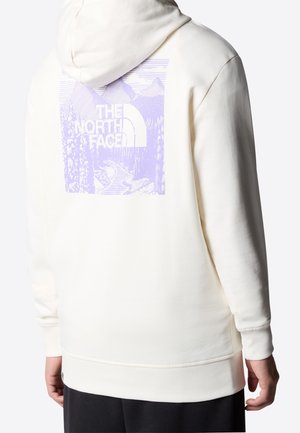 Persoon draagt een witte hoodie met een paarse berg, bomen, riviergrafiek en de tekst "THE NORTH FACE" op de rug.