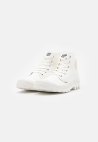 Sneaker alte bianche in tela con punta tonda, lacci, suola in gomma bianca testurizzata e logo sul lato.