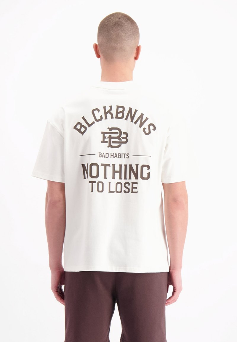 Witte katoenen t-shirt met een grote bruine grafische print op de achterkant met tekst: "BLCKBNNS BAD HABITS NOTHING TO LOSE." Korte mouwen, ontspannen pasvorm.