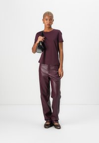 T-shirt bordeaux à manches courtes, associé à un pantalon en cuir bordeaux et un sac à main noir. Les chaussures présentent un design à imprimé léopard.