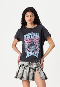 T-shirt noir à manches retroussées, arborant un design graphique bleu et rose avec l'inscription "RÊVERIE MYSTIQUE". Associé à une jupe plissée à longueur de genou.