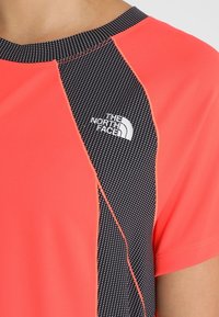 Červené a černé sportovní tričko s tečkovanou texturou na panelu, kulatým výstřihem a bílým logem na levé straně hrudi.