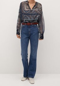 Blouse bleu marine translucide à motif cachemire, assortie à un jean bleu taille haute et une ceinture marron. Chaussures avec un design en maille de couleur claire.