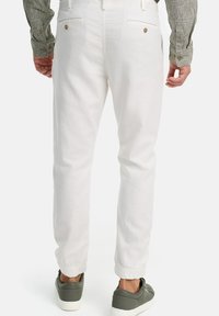 Pantalones blancos de mezcla de algodón con un diseño ajustado, puños elásticos y dos bolsillos traseros con botones, combinados con zapatillas verdes.