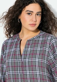 Camicia a scacchi grigia con linee rosa e bianche, dotata di scollatura a V e maniche lunghe. Realizzata in un tessuto morbido e con una texture piacevole.