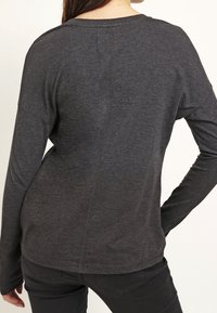 Dunkelgraues Langarmshirt mit Rundhalsausschnitt, das eine Nahtdetails an der Rückseite und taillierte Ärmel aufweist. Hergestellt aus weichem, leichtem Stoff.