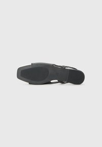 Zapato negro con un material superior liso y un diseño de tiras delgadas. La suela es de goma con un agarre texturizado para mayor tracción.