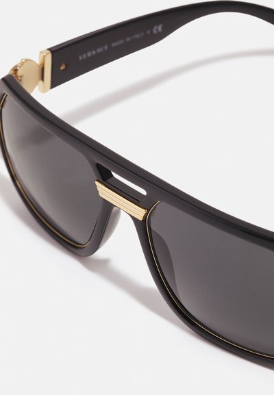 Occhiali da sole neri con lenti scure, rifiniture color oro sugli steli e un design geometrico. Realizzati in plastica con una superficie liscia.