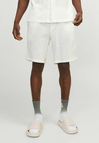 Hvide teksturerede shorts med en afslappet pasform, parret med grå gradient sokker og beige slidesandaler. Bemærkelsesværdigt blødt materiale og søm detaljer.