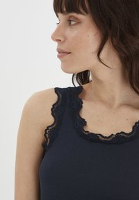 Tumesinine ribaga tank top, mille kaeluse ja rihmade ääres on pitsäär. Pehme tekstuur, liibuv disain ja dekoratiivsed lainelised servad.
