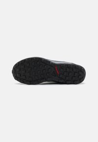 Semelle en caoutchouc noir d'une chaussure avec un motif texturé pour une meilleure adhérence. Présente un logo "Traxion" rouge. La zone des orteils est arrondie avec une finition lisse.