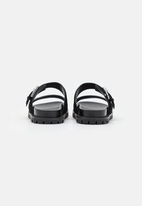 Pair of black flat sandals with two straps and silver buckles, viewed from the back on a white background.