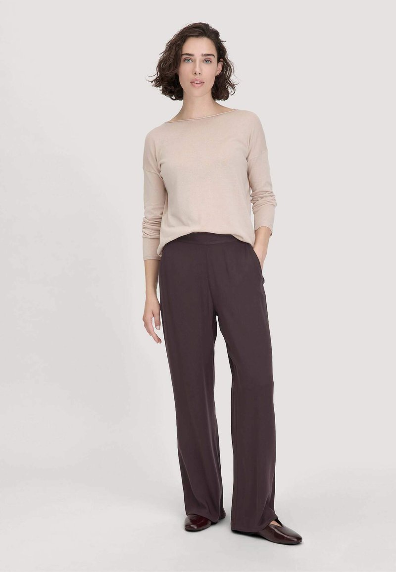 Hellbeige langärmliges Oberteil kombiniert mit dunkelvioletten, fließenden Hosen. Die Kleidungsstücke haben einen lockeren Schnitt und minimale Details für einen sauberen Look.