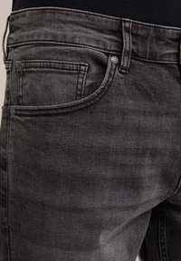 Nära bild av svarta denimjeans som visar framfickan, bältesöglor och metallnitar på en person som bär en svart topp.