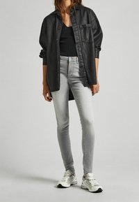 Camisa de denim oversize negra, top ajustado negro, jeans skinny gris claro y zapatillas blancas con acentos grises. Texturas suaves y diseño casual.