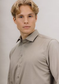 Lys brun skjorte med lange ermer, knappelukking og spredt krage. Glatt tekstur med subtile mønstre.