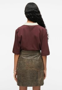 Korte mouwen, bordeauxrood t-shirt met een crème kleurige kraag, gecombineerd met een bruine leren rok met twee achterzakken en een verweerd uiterlijk.