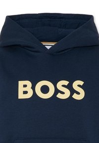 Felpa navy in cotone, con un grande logo "BOSS" color crema. Cappuccio con cordino e tasca a marsupio anteriore. Texture liscia.