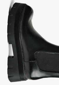 Cizme negre de gleznă din cauciuc cu finisaj neted, talpă groasă și panou elastic lateral. Design minimalist fără modele sau accente suplimentare.