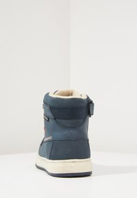 Bota alta azul con forro de piel sintética, suela de goma y cierre de cremallera. Logo en el lateral y acentos blancos contrastantes en la parte superior.
