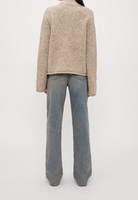 Stickad beige tröja med rak passform, texturerad tyg och hög krage, matchad med ljusblå vida jeans med bakfickor.