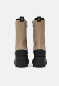 Bottes en cuir beige chevilles avec une semelle en caoutchouc noir, une fermeture éclair sur le côté et des accents contrastants au talon et aux orteils. Fini texturé.