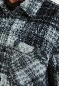 Fleecejacka i grå och svart rutigt mönster, med en texturerad yta, knappstängning framtill och en krage.