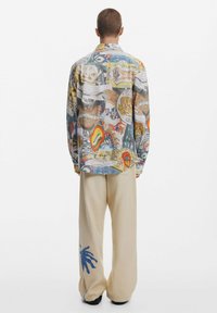 Multicolored button-up shirt with graphic patterns and illustrations. Loose-fitting cream trousers featuring a blue palm design.