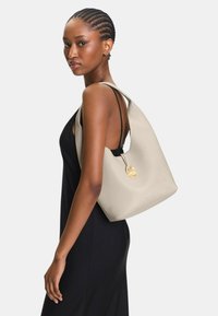 Borsa hobo in pelle beige con una forma morbida, caratterizzata da dettagli in metallo dorato e una ampia tracolla. Texture liscia, design minimalista.