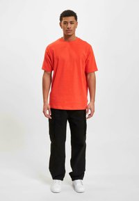 Oranges Baumwoll-T-Shirt mit Rundhalsausschnitt, lockerer Passform und kurzen Ärmeln, kombiniert mit schwarzen Cargo-Hosen und weißen Sneakers.